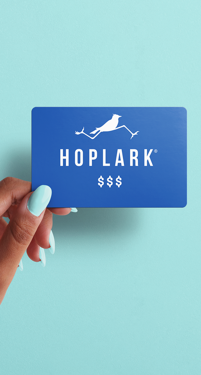 Hand holding a blue gift card with 'HOPLARK' logo against a light blue background