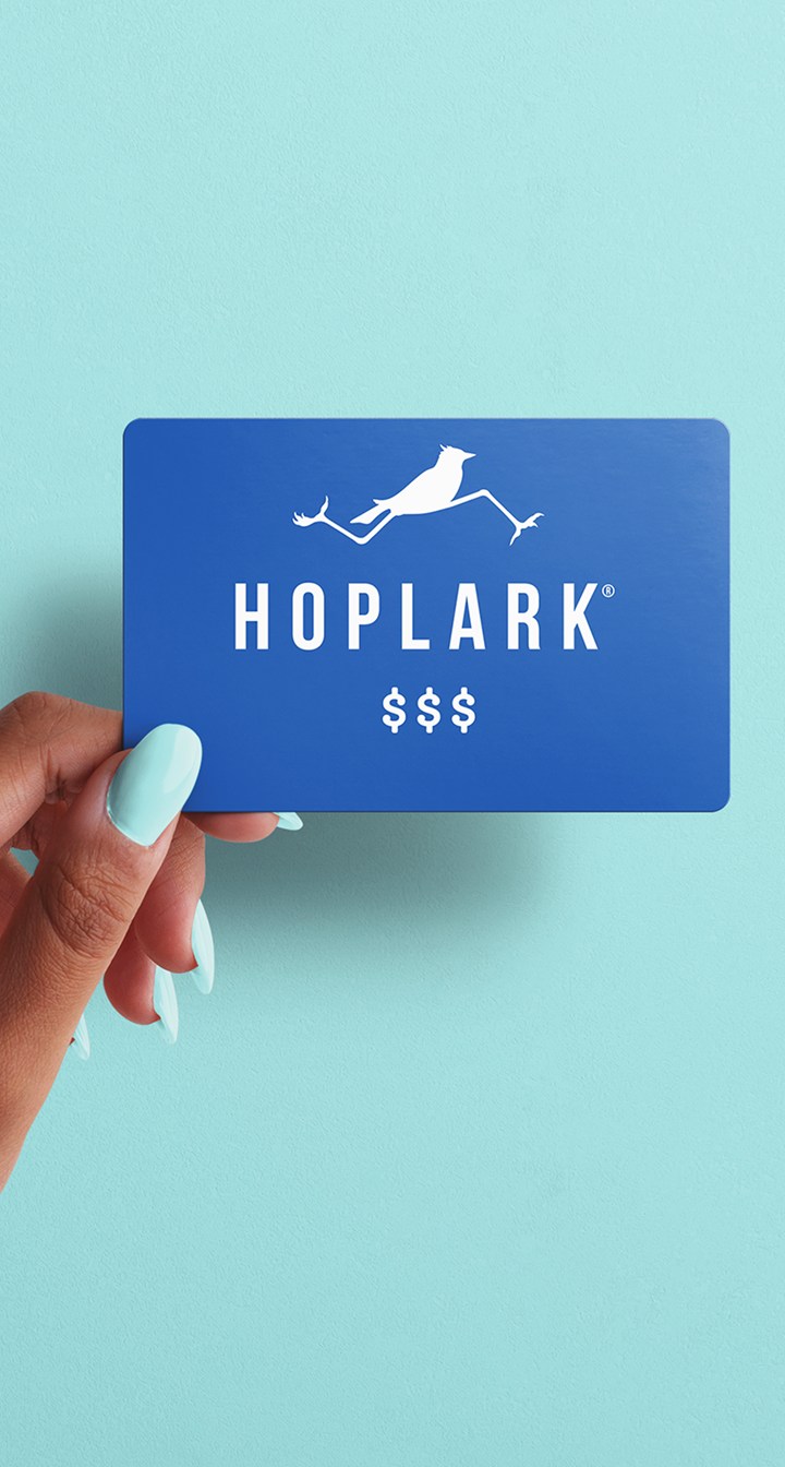 Hand holding a blue gift card with 'HOPLARK' logo against a light blue background